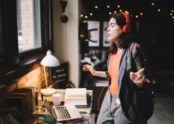 Young Latinx woman sitting at the desk in her Los Angeles apartment, receiving happy news over the social networks or just having a nice day, dancing to the music.